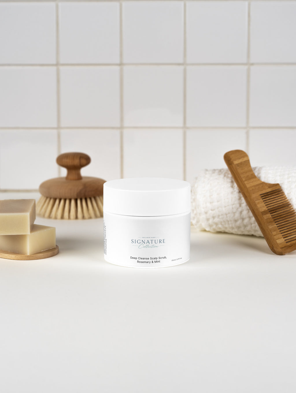 Cosmetic jar with scrub, soap, and wooden tools on a white surface with tiled wall background